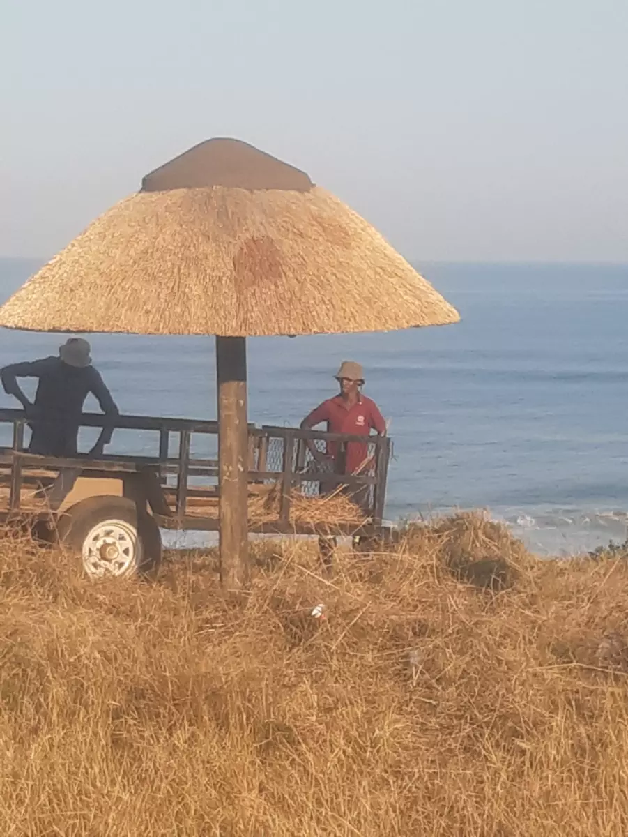 Two workers by a thatched umbrella and trailer overlooking the ocean